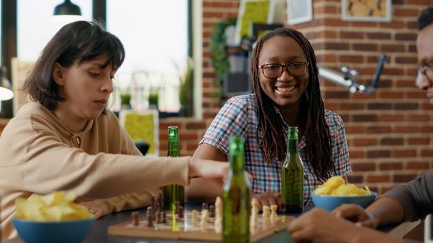 Portrait of female person smiling and playing board games with group of friends at home gathering. Young woman having fun and relaxing with chess match and alcoholic beer drinks.