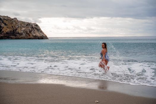 A plump woman in a bathing suit enters the water during the surf. Alone on the beach, Gray sky in the clouds, swimming in winter