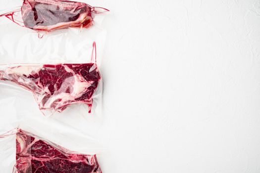 Fresh premium Dry aged marbled steak in a vacuum pack set, tomahawk, t bone and club steak cuts, on white stone background, top view flat lay, with copy space for text