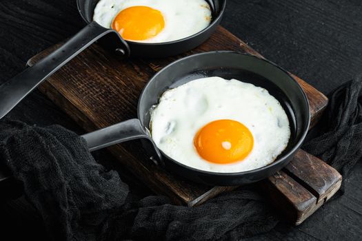 Fried eggs with cherry tomatoes and bread for breakfast in cast iron frying pan, on black wooden table background