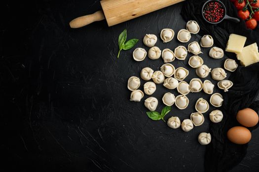 Tasty raw tortellini with flour and basil set, on black background, top view flat lay , with copyspace and space for text