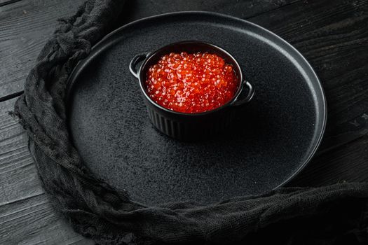 Red caviar black bowl, on black wooden table background