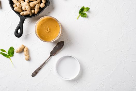 Peanut paste in an open jar and peanuts set, on white stone table background, top view flat lay, with copy space for text