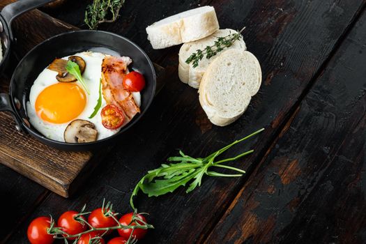 Fried eggs with cherry tomatoes and bread for breakfast in cast iron frying pan, on old dark wooden table background , with space for text copyspace