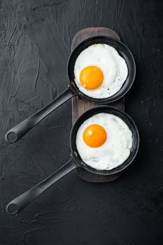 Fried eggs with cherry tomatoes and bread for breakfast in cast iron frying pan, on black background, top view flat lay