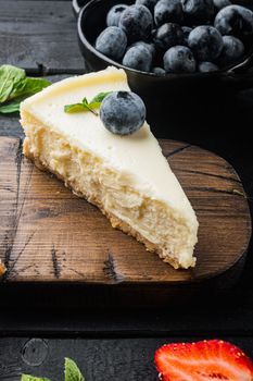 Portion of cheesecake with berrie, on black wooden table background