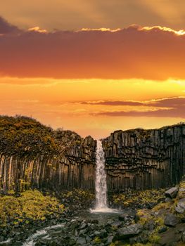 Svartifoss waterfall in Skaftafell National Park under bright orange sky