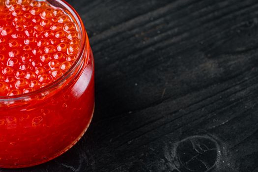 Red caviar jar, on black wooden table background with copy space for text