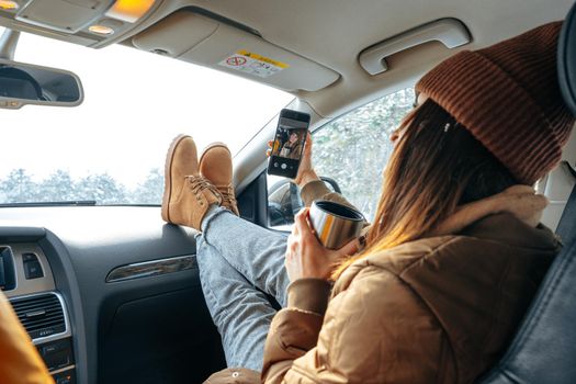 Beautiful young woman wearing warm clothes sitting in car while winter road trip, close up