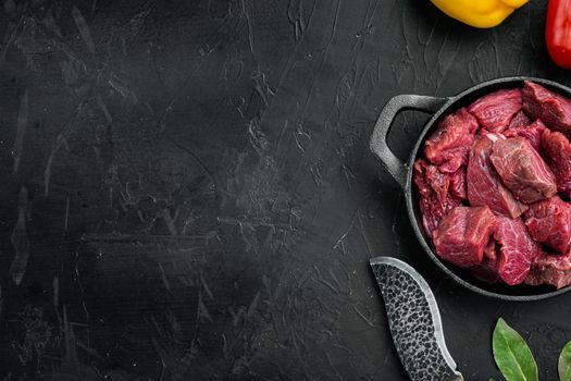 Raw veal beef for stew set, in cast iron frying pan, on black stone background, top view flat lay, with copy space for text