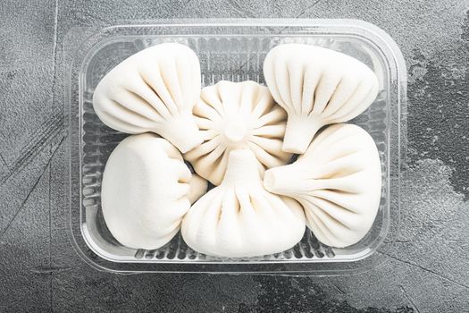 Stuffed dumplings, manti of dough and minced set, in plastic tray, on gray stone background, top view flat lay