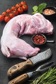 Fresh raw rabbit with olive oil, rosemary, peppers set, on black stone background