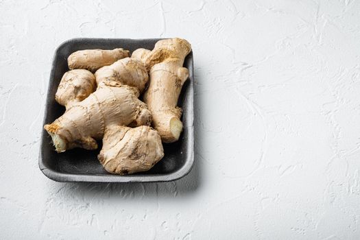 Ginger root set, in plastic market container, on white stone background, with copy space for text