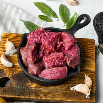 Fresh raw chopped beef set, in cast iron frying pan, on white stone surface, square format