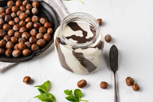 Chocolate spread or nougat cream with hazelnut set, on white stone table background, with copy space for text