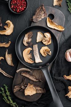 Dried mushrooms set in cast iron frying pan, on black background, top view flat lay