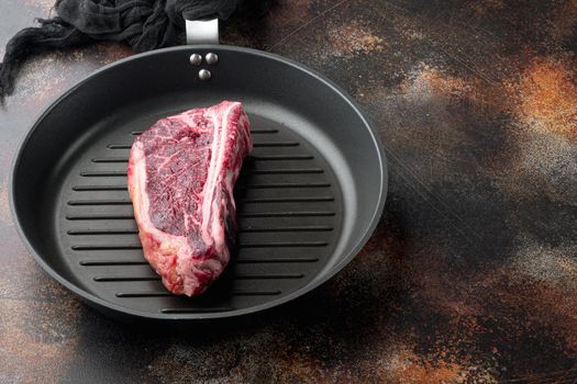 Raw beef meat marbled dry aged Club or striploin on the bone steak set, on frying cast iron pan, on old dark rustic background, with copy space for text