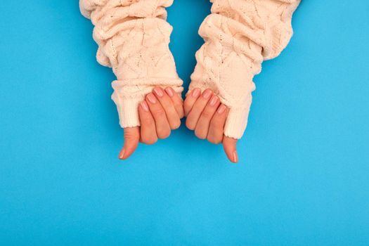 Neat manicure female hands sweater sleeves nude naturel on a blue background