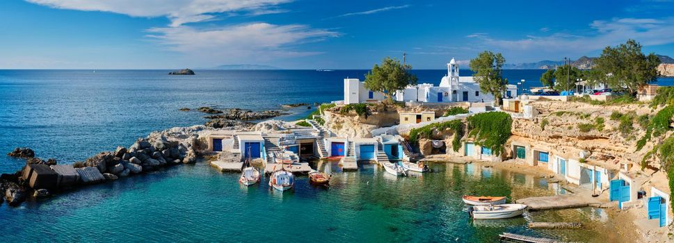 Panorama of typical Greece scenic island view - small harbor with fishing boats in crystal clear turquoise water, traditional white houses church. Mandrakia village, Milos island, Greece.