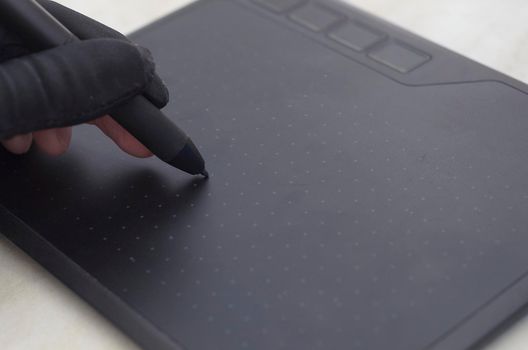 Graphic designer's hand in a black glove draws on the workspace of a graphics tablet,close up.