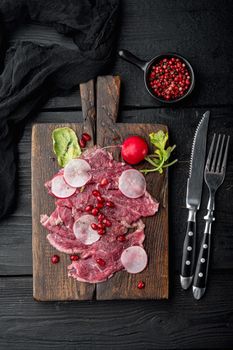 Classic beef carpaccio set, with Radish and garnet, on wooden serving board, on black wooden table background, top view flat lay