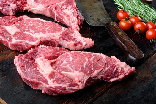 Raw rib eye beef marbled meat steak with pepper and herbs set, and old butcher cleaver knife, on old dark wooden table background