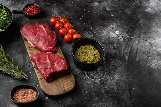 Raw beef meat steak with herbs set, on black dark stone table background, with copy space for text