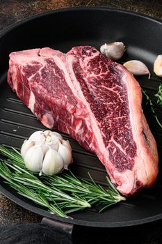 Raw T-bone Steak for grill or BBQ with ingredients set, on frying cast iron pan, on old dark rustic background