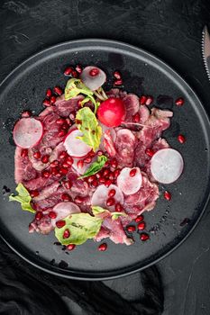 Fresh carpaccio salad with wine vinegar set, with Radish and garnet, on plate, on black stone background, top view flat lay