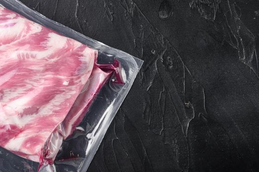 Pork ribs in a vacuum bag set, on black stone background, top view flat lay, with copy space for text