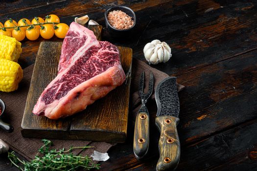 Big raw porterhouse steak with spices and ingredients set, on old dark wooden table background, with copy space for text