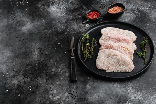 Uncooked Wiener Schnitzel, breaded steak ready to cook set, on black dark stone table background, with copy space for text