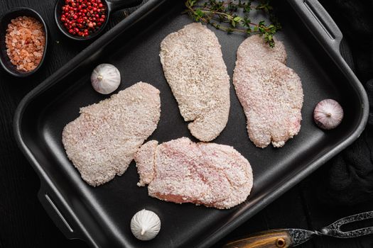 Raw chicken schnitzel in breadcrumbs, on black wooden table background, top view flat lay