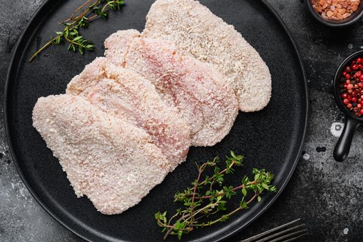 Raw chicken schnitzel in breadcrumbs, on black dark stone table background, top view flat lay