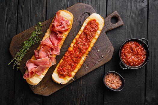 Crusty toast with fresh tomatoes and cured ham, on black wooden table background, top view flat lay