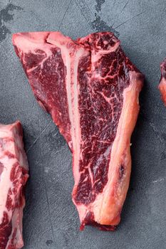 Prime cut tender raw t-bone steak for a BBQ set, on gray stone background, top view flat lay