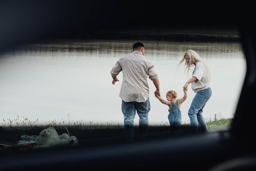 Happy Young Family with Kid Holding by Hands Together and Enjoying Weekend Outside the City, View Through Window Inside of Car