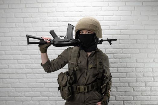 Ukrainian girl soldier in a helmet and military ammunition with a Kalashnikov assault rifle on the background of a brick wall