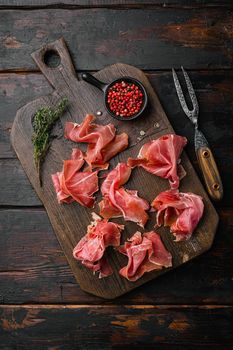 Slices of prosciutto di parma or jamon serrano, on old dark wooden table background, top view flat lay, with copy space for text