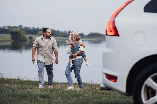 Happy Young Family Having Fun Time Outdoors Near the Lake, Mom and Dad with Their Toddler Daughter Enjoying Road Trip on Car
