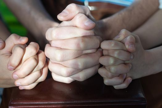 Two Christian people are praying for young man friends on wood table at church prayer room to encourage and support him in his problem and spiritual growth, small prayer group and fellowship concept