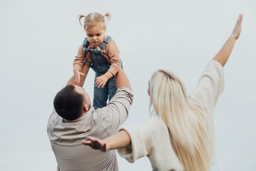 Young Family Having Fun Time Outdoors, Father Holding His Little Daughter in Arms Over Head, Mother Imitating Plane