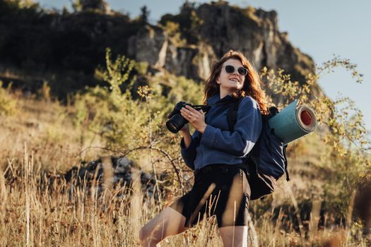 Portrait of Young Travel Woman in Sunglasses, Holding Digital Camera in Hands and Looking Away with a Smile, Female Traveler Enjoy Her Best Solo Hike