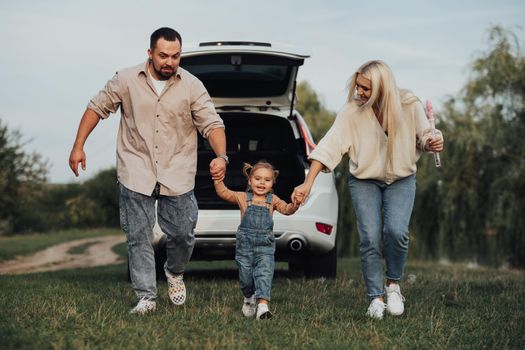 Happy Family Having Fun Outdoors, Young Parents with Their Little Daughter Playing Together