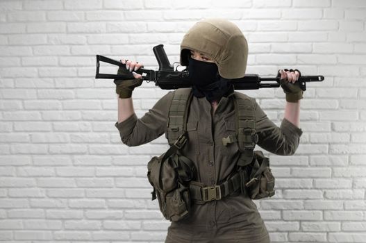Ukrainian girl soldier in a helmet and military ammunition with a Kalashnikov assault rifle on the background of a brick wall