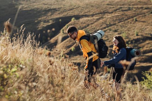 Travel Couple Man and Woman with Backpacks and Camping Mat Holding by Hands Moving on Hill During Sunset