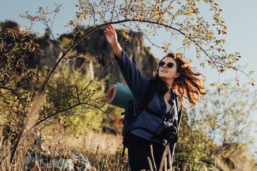 Cheerful Young Travel Woman in Sunglasses With Backpack with Camping Mat and Digital Camera on Strap Making Her Way Through the Thickets During Her Hike