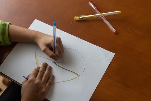 Childrens hand with pencil draws the heartl.