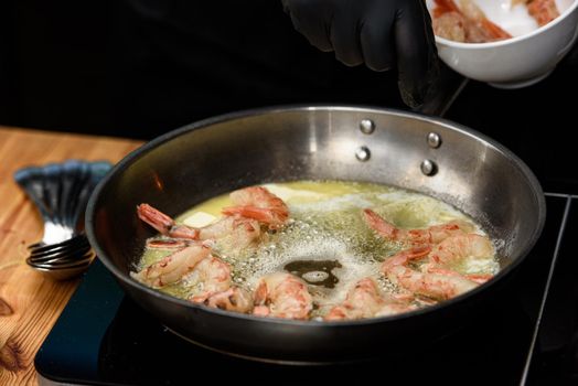 Fried red shrimps with garlic in olive oil on black pan on stove. Step by step cooking of shrimp pasta.