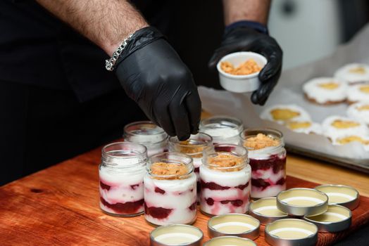 Chief preparing dessert in a glass cup, with Jello, yogurt and topping. Mini desserts.